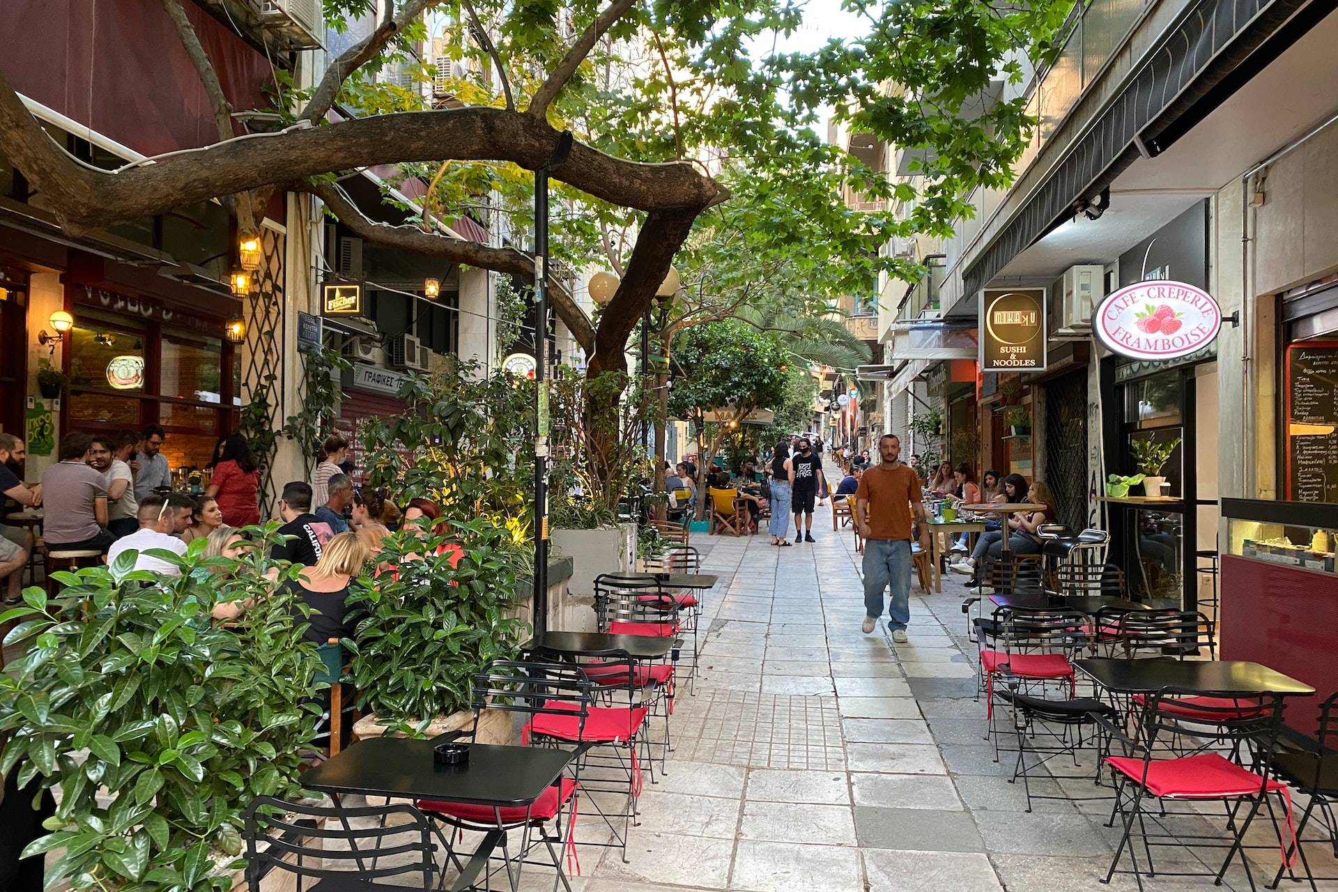 a group of people walking down a sidewalk next to tables and chairs