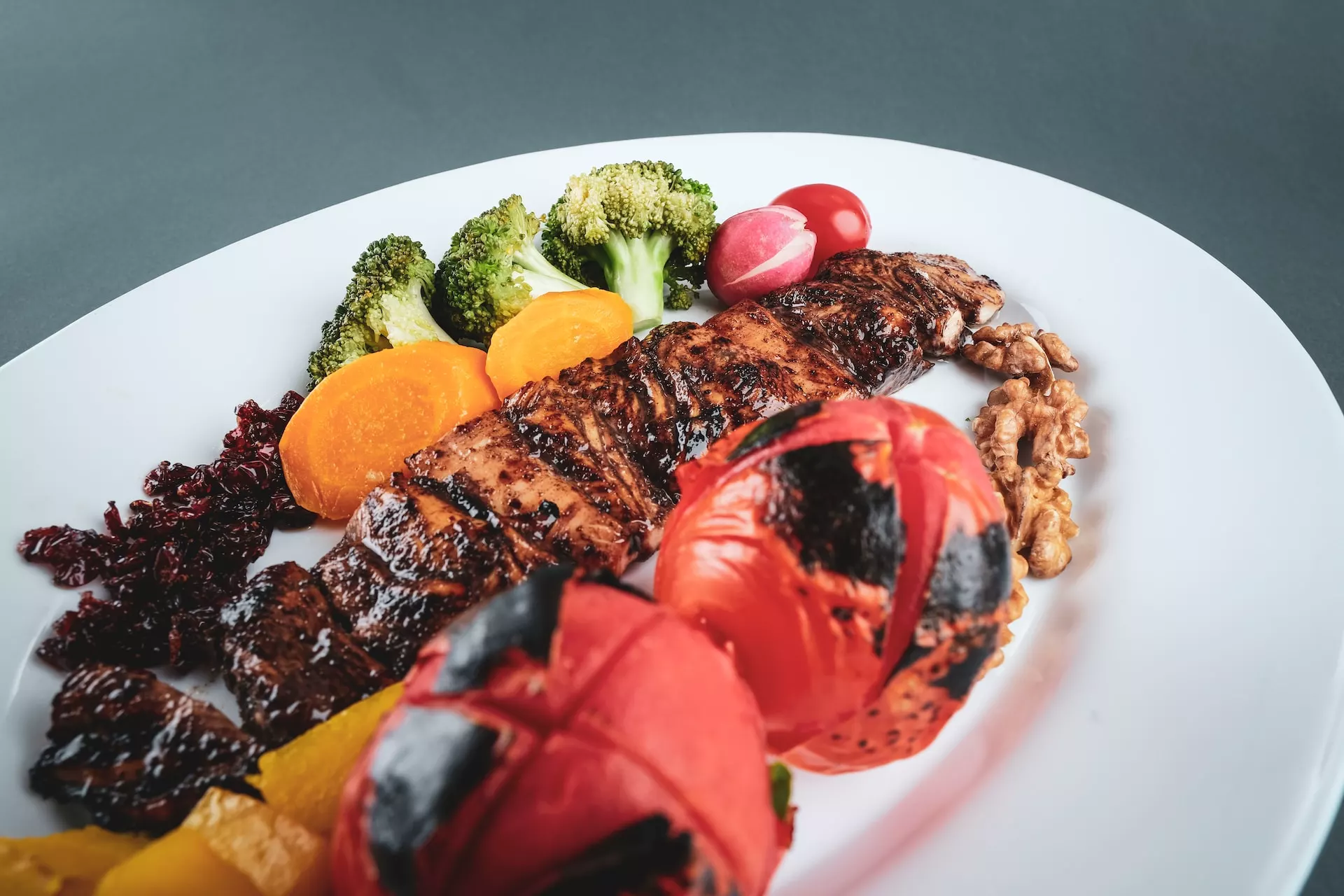grilled meat with sliced tomato and green vegetable on white ceramic plate